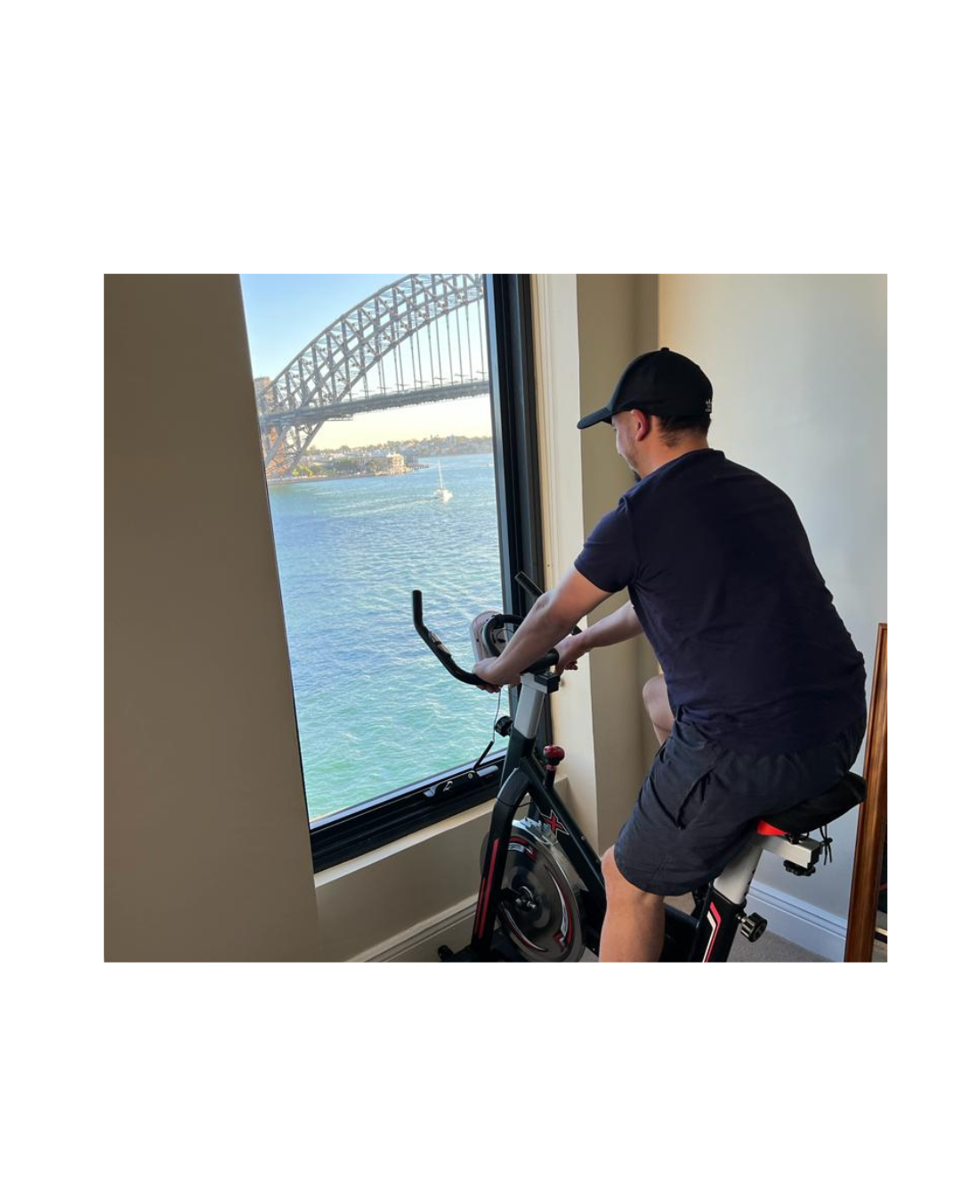 Client using stationary bike for physiotherapy exercise near large window with physiotherapist monitoring progress