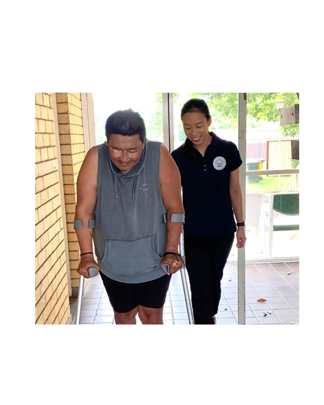 Physiotherapist walking alongside elderly client using forearm crutches during outdoor mobility training