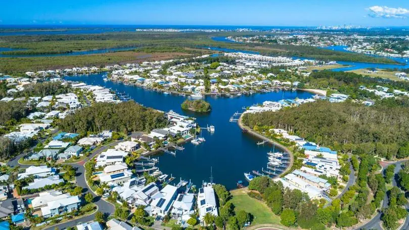 Aerial view of the waterfront residential community in Coomera Waters, showcasing modern homes, private docks, and canals surrounded by greenery and waterways on the northern Gold Coast.