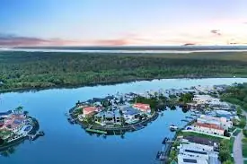 Aerial view of Paradise Point, Gold Coast, featuring waterfront homes, private docks, and surrounding natural reserves at sunrise.