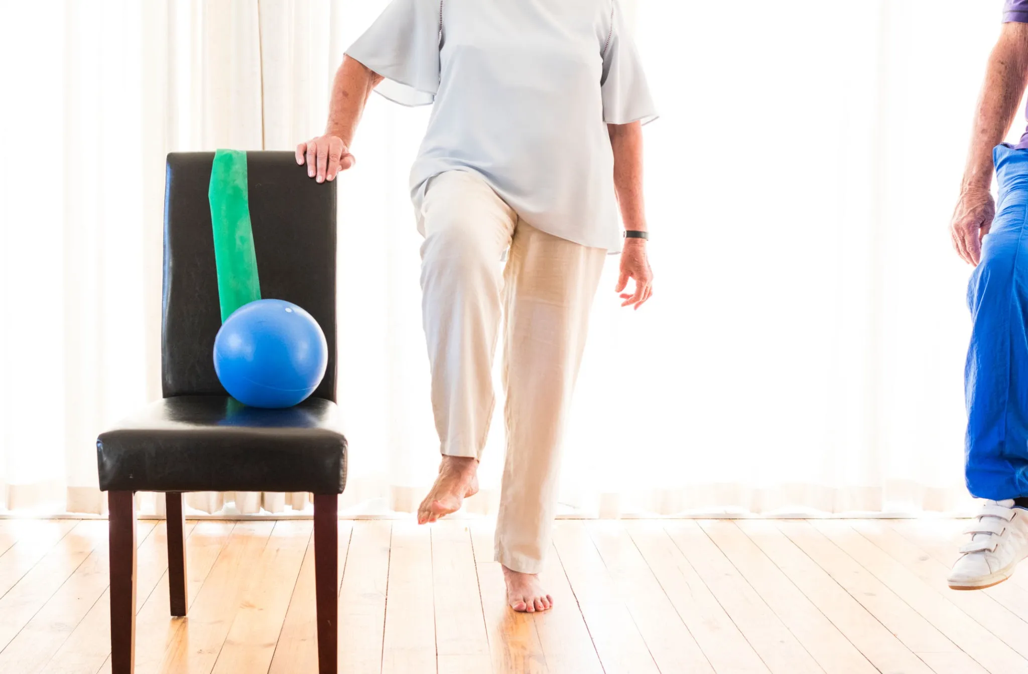 Close-up of physiotherapist guiding senior through balance exercises using household furniture for support.