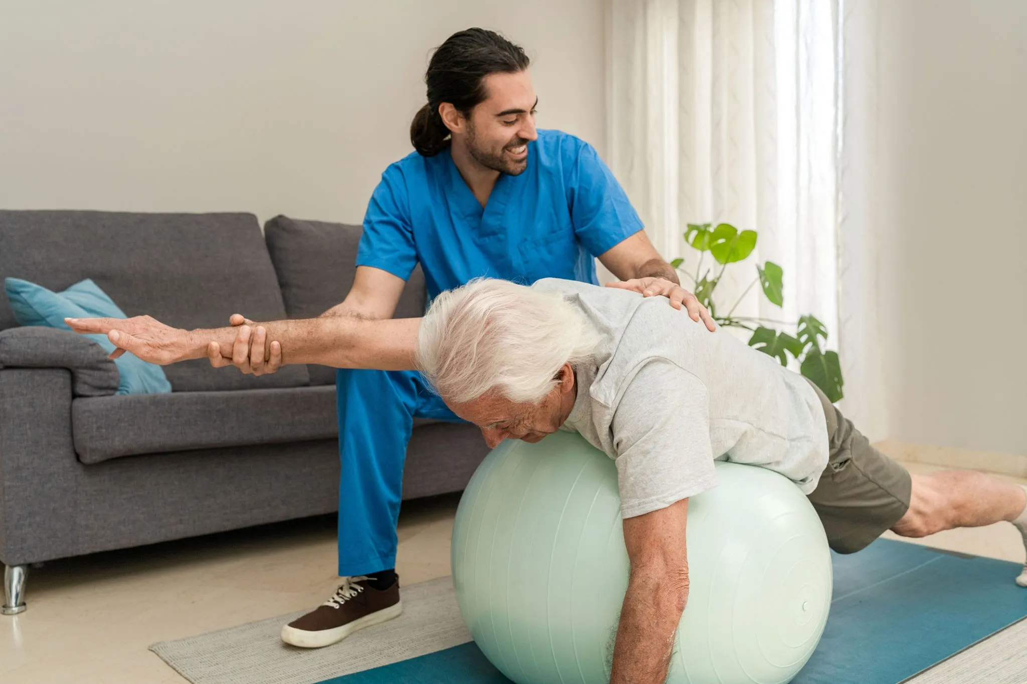 Physiotherapist helping senior client with balance exercises in home environment, showing functional training.