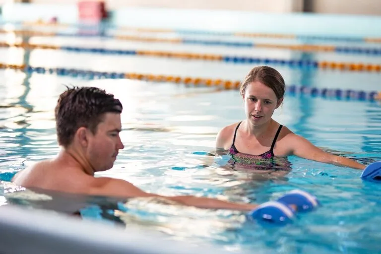 Two people engaging in hydrotherapy exercises in a swimming pool with lane dividers in the background