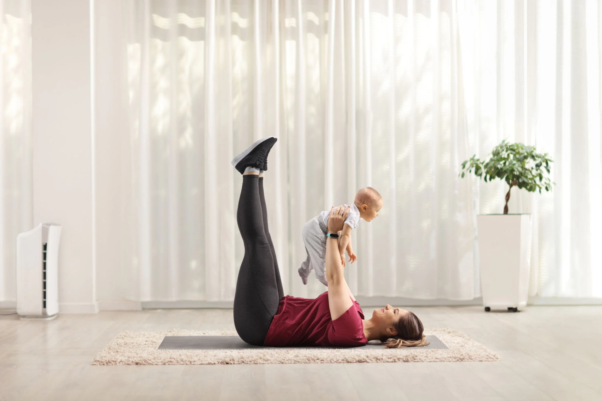 A new mother doing core exercises on a mat at home with baby nearby in a bassinet