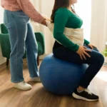 A pregnant woman doing gentle home stretches with a physiotherapist beside