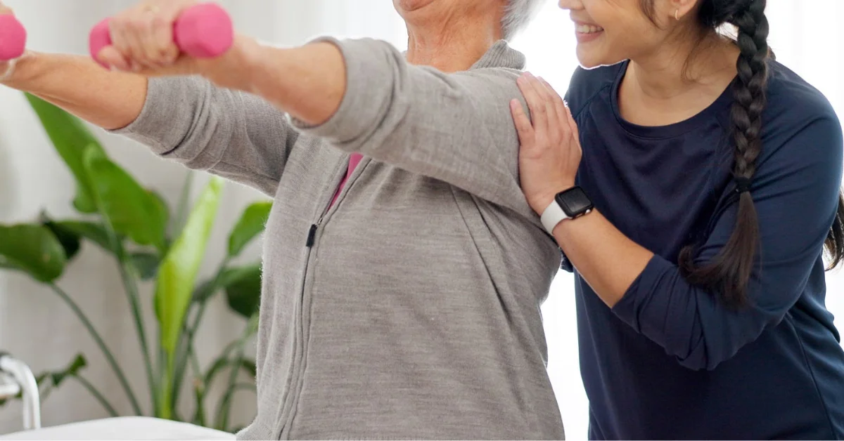 Senior woman smiling while completing a gentle exercise routine at home with a physiotherapist providing encouragement and support (1)