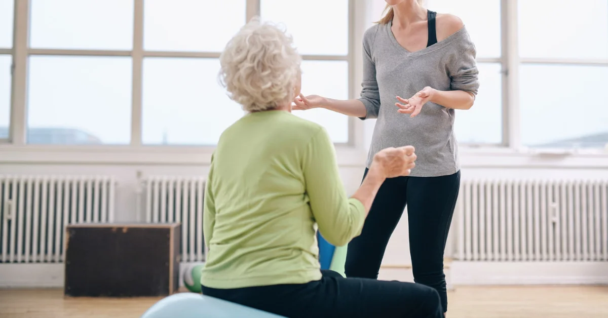 Senior woman smiling while completing a gentle exercise routine at home with a physiotherapist providing encouragement and support