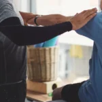 Warm, professional image of a physiotherapist working with an elderly patient in a comfortable home setting, showing gentle guidance during a balance exercise
